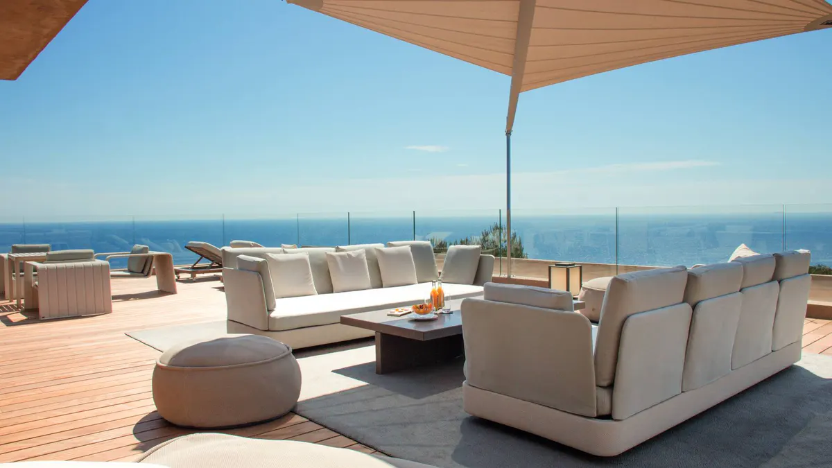 Oceanside terrace with cream sofa and wooden umbrella in sunlight