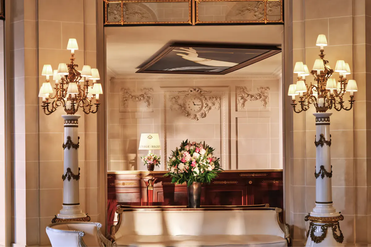 An ornate entrance hall with gilt mirrors, classical sculptures, and marble columns