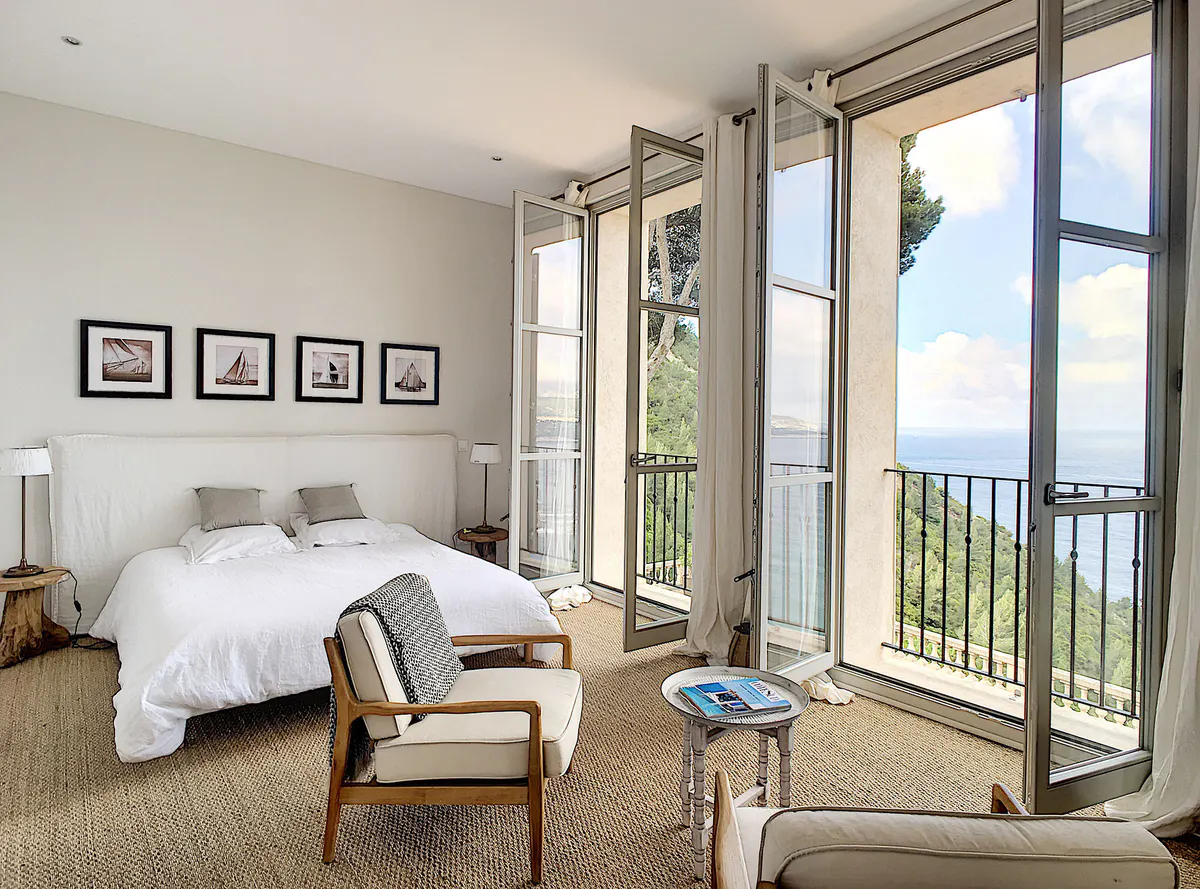 Sunlit bedroom with large glass doors opening to sea-view terrace and natural furnishings
