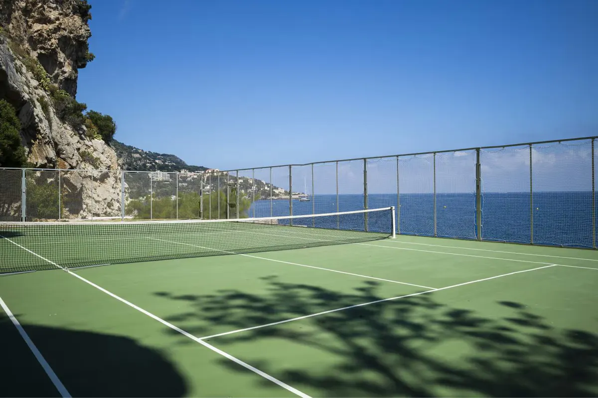 A tennis court with bright green surface and nets overlooking the sea