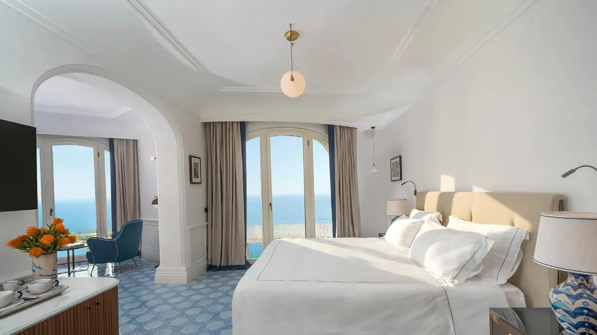 Spacious bedroom with arched ceiling, dual wall sconces, and seating nook overlooking sea
