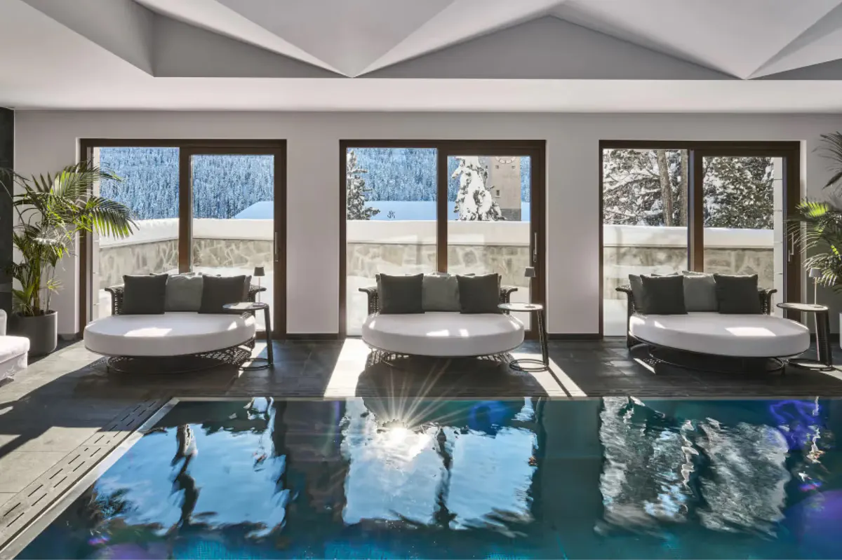 Indoor pool with blue water, large windows, loungers, and alpine landscape beyond