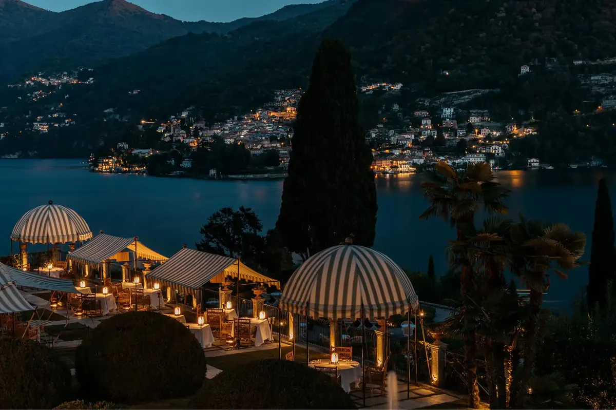 Outdoor terrace at dusk with illuminated dome tents, lake town lights below
