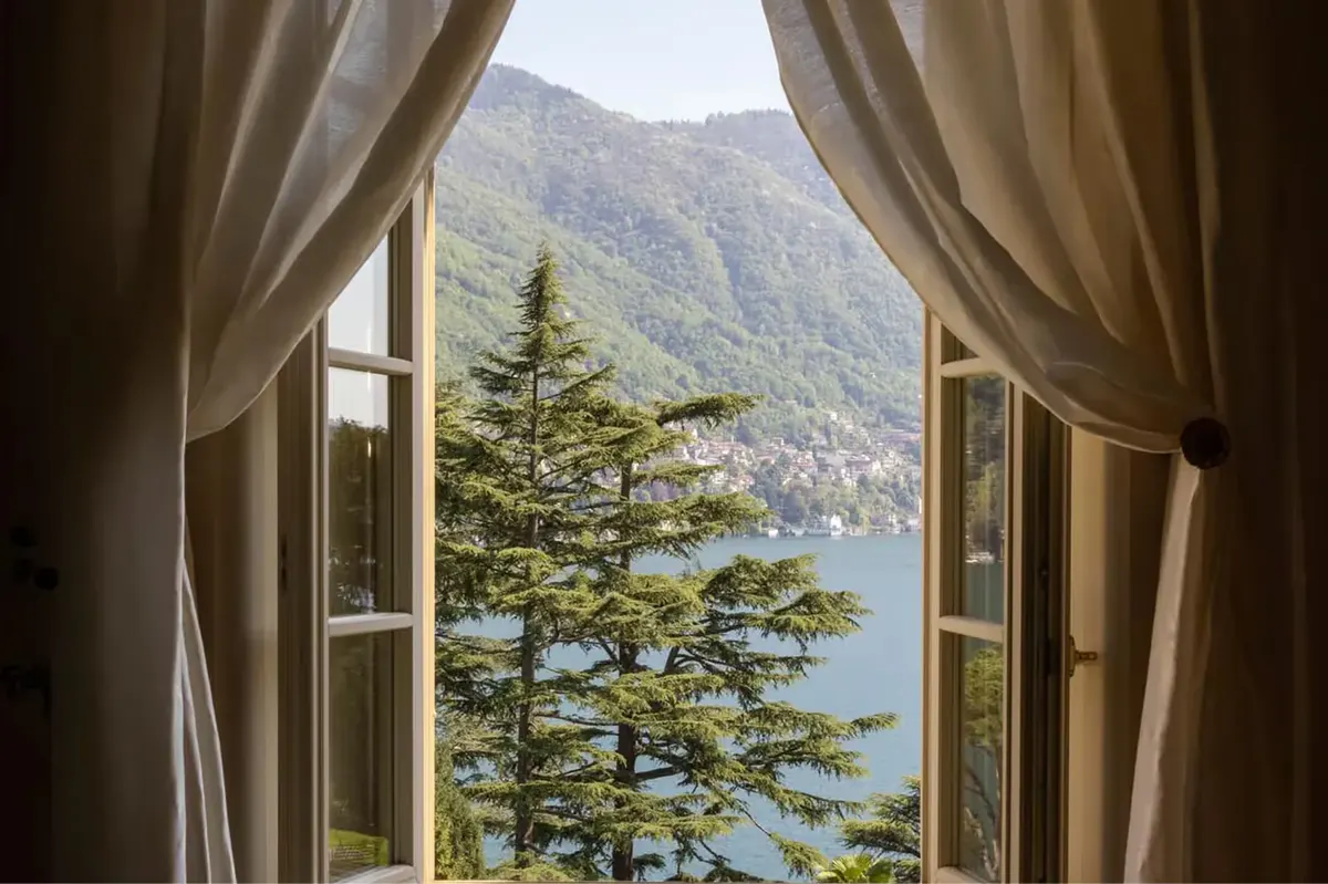 Open French doors framing a lake and cypress trees beyond sheer curtains