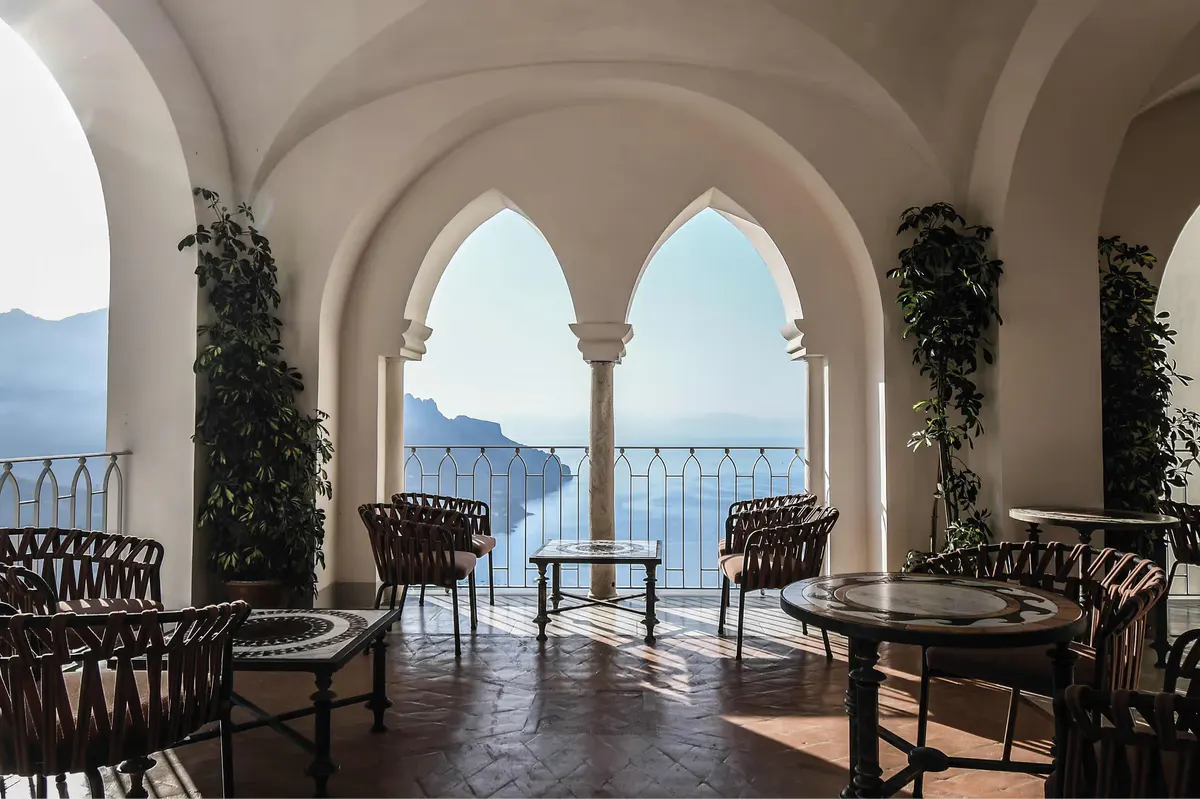 Arcade pavilion with ornate columns, stone seating, painted ceiling panels, and panoramic coastal view