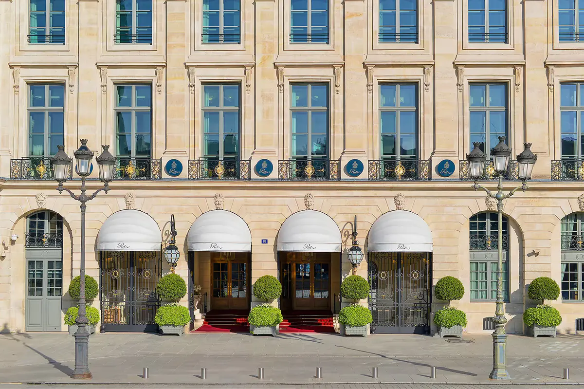 The Ritz Paris facade on Place Vendôme with golden stone, arched entrances, and topiary-lined forecourt