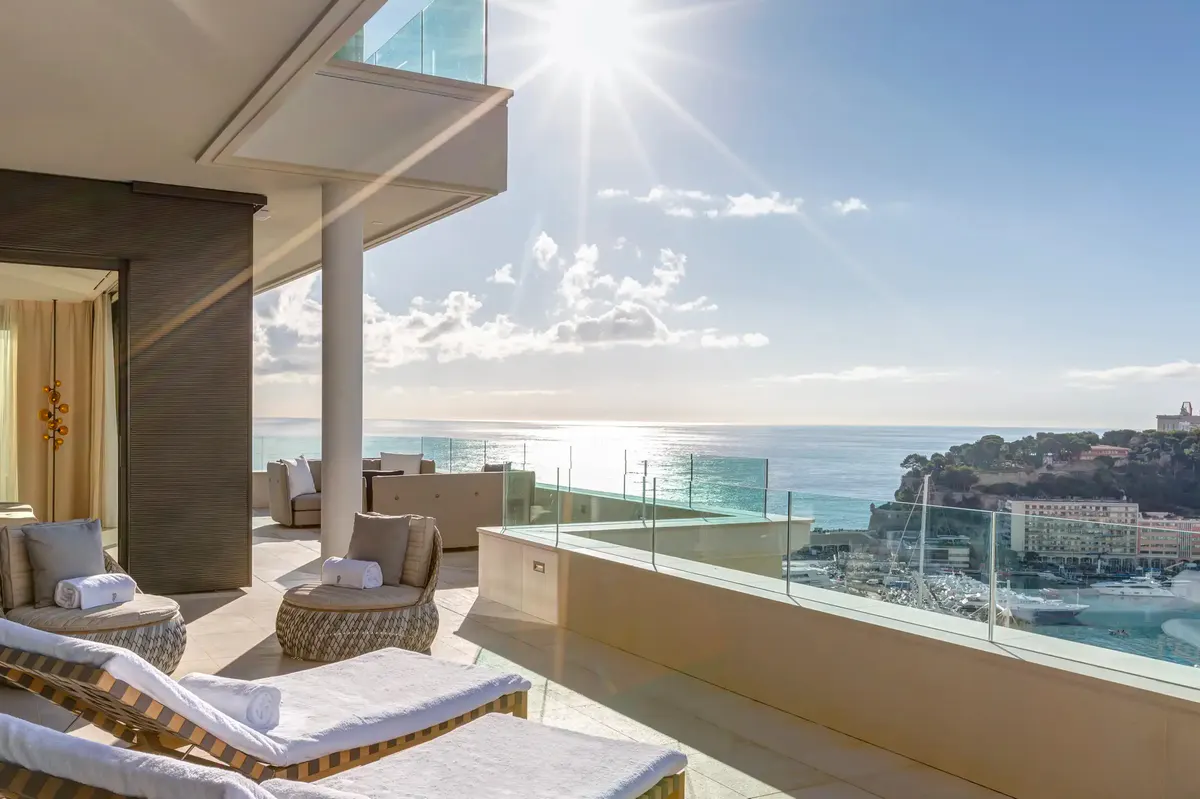 Suite bedroom with white bedding and floor-to-ceiling balcony overlooking sea