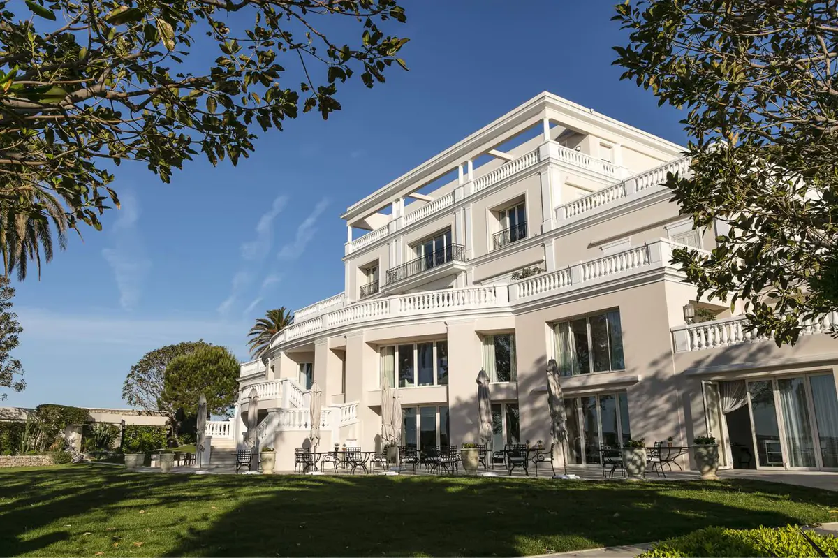 A neoclassical white villa with balconies overlooking manicured gardens