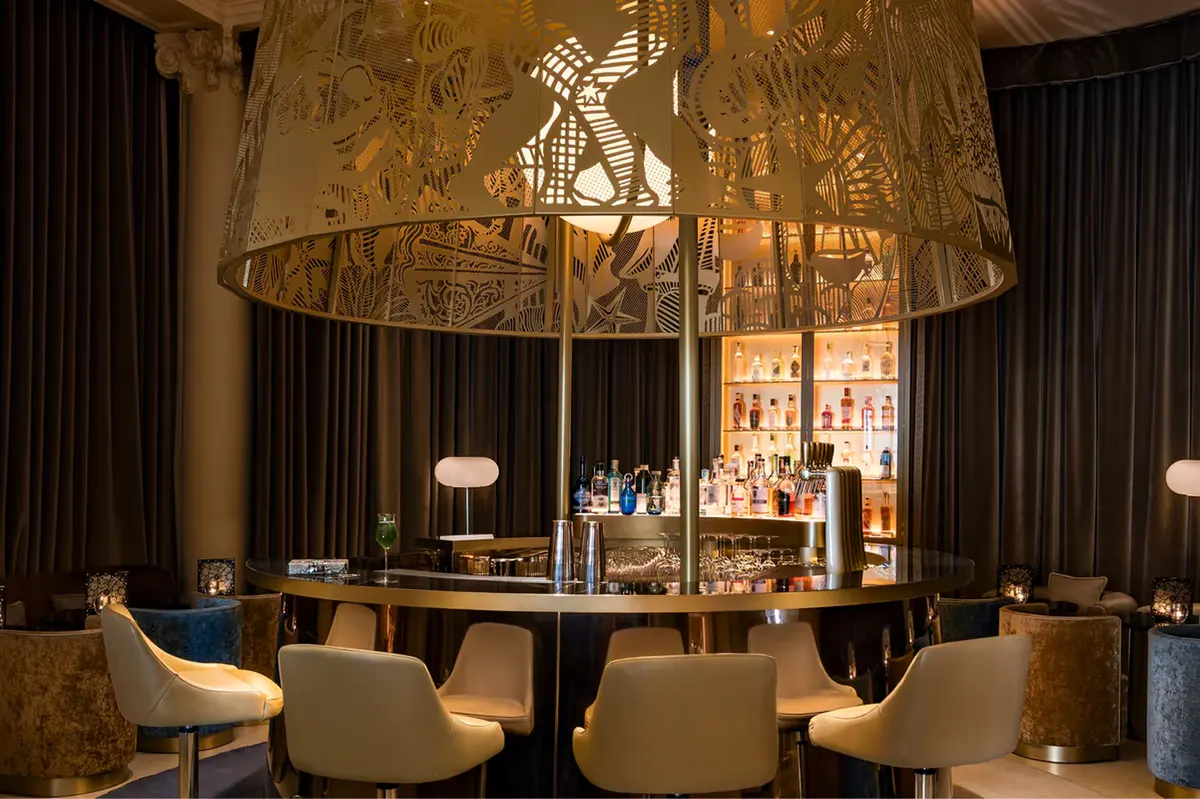 An elegant bar area with gilt accents, cream chairs, and ambient lighting fixtures
