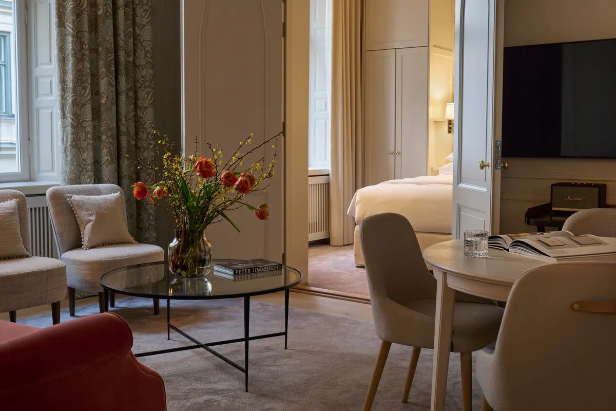 Suite living area with red accent seating, bedroom beyond, and arranged floral arrangement