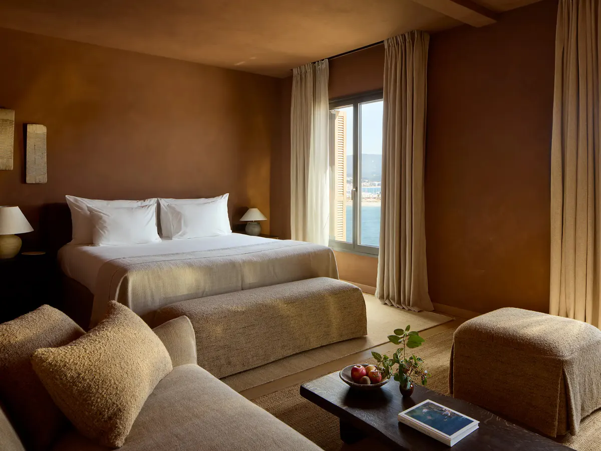 A corner suite bed faces floor to ceiling windows over the harbor and distant hills
