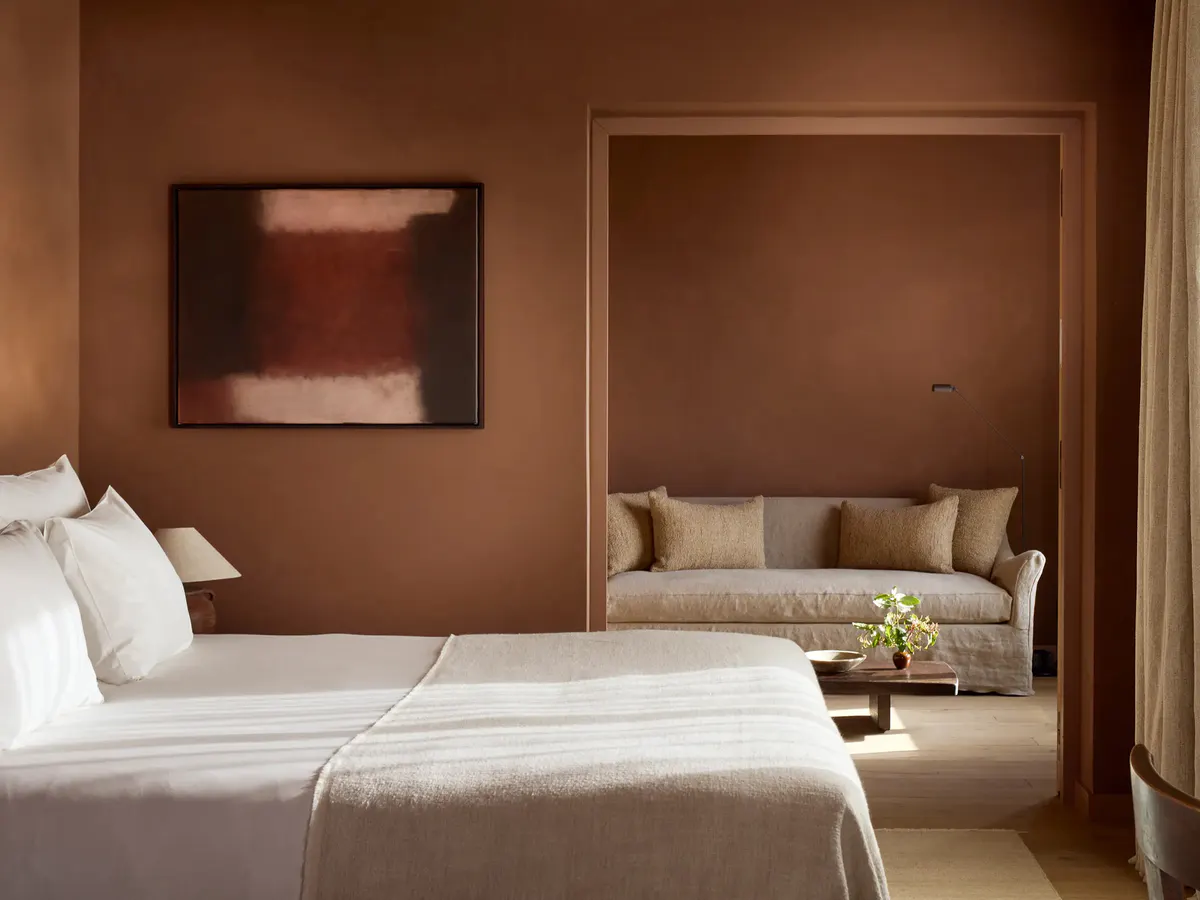A terracotta suite pairs a framed abstract canvas with a linen sofa nook beyond the bed