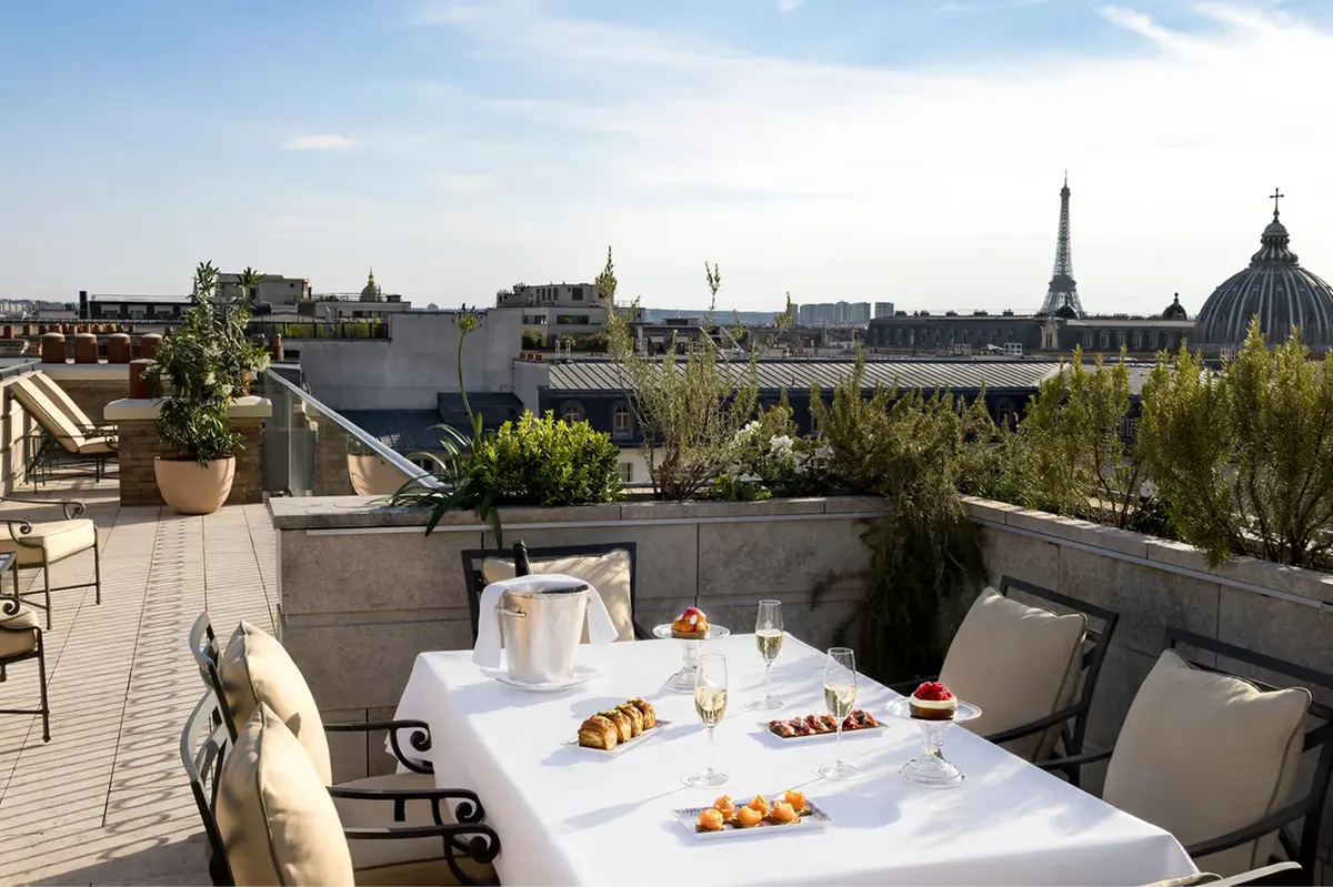 A rooftop terrace with white dining table, gray seating, and sweeping Paris skyline views
