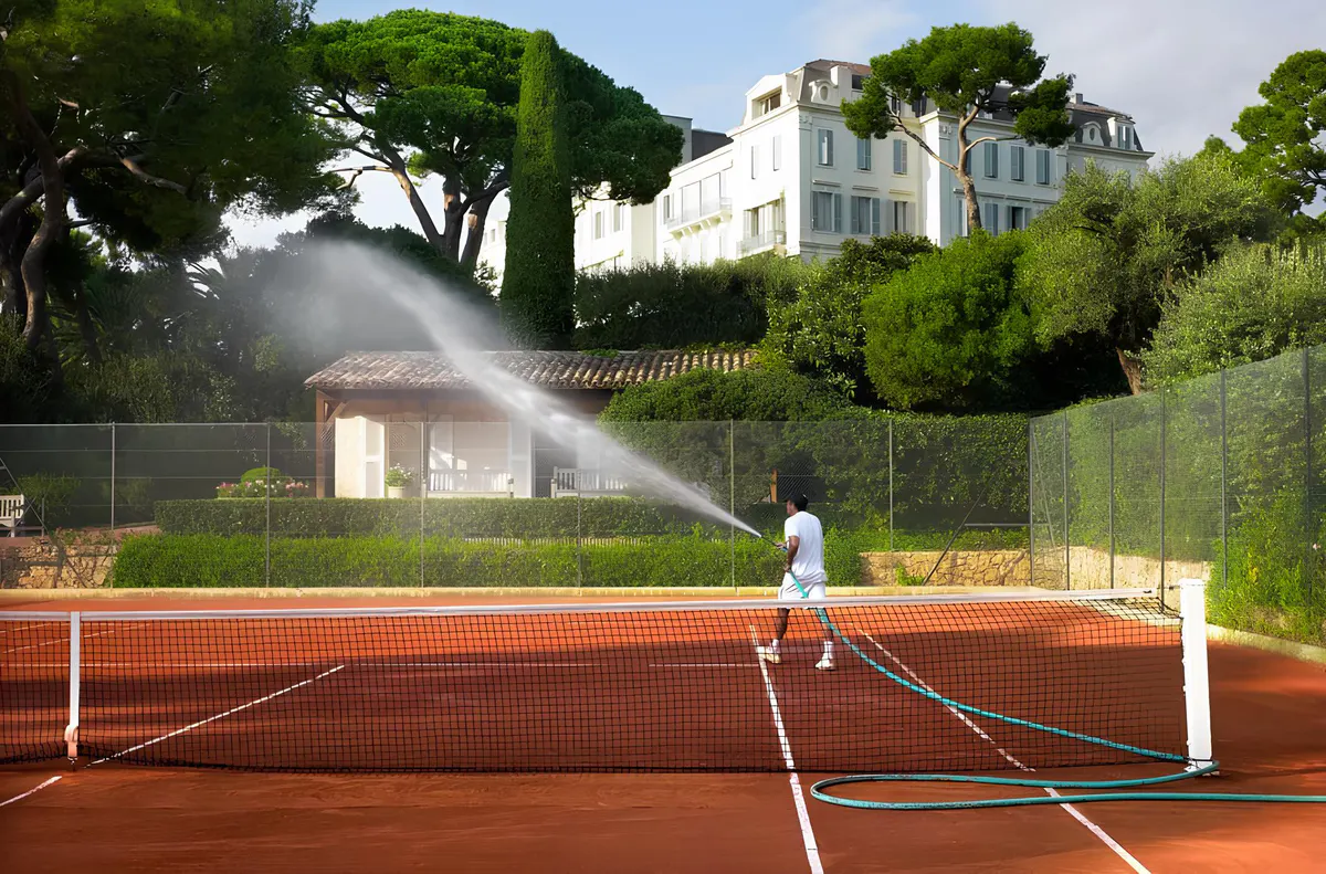 An aerial view of red clay tennis courts set in pine forest on the Riviera estate