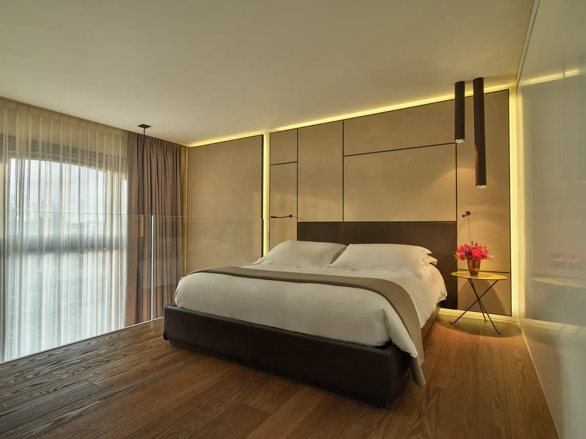 Master bedroom with upholstered headboard, backlit panels, and floor-to-ceiling drapes