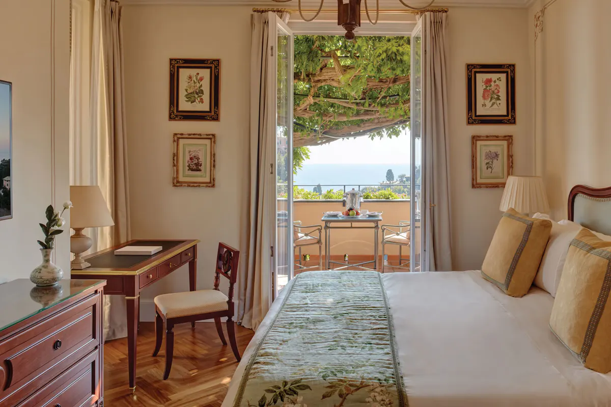 A bedroom with open doors to a sea-view terrace and classical Italian furnishings