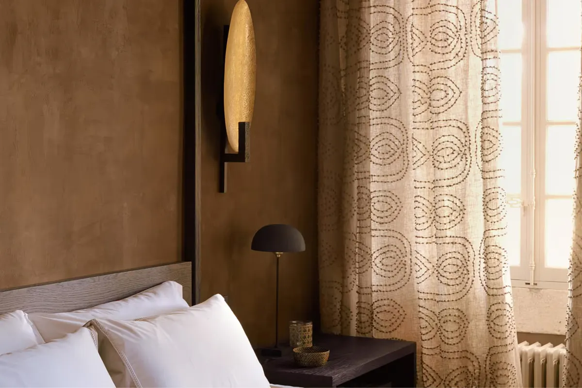 Bedroom corner with warm tan walls, gold patterned curtains, and light wood nightstand