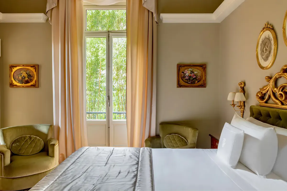 Bedroom with tall windows, gilt-framed mirrors, and upholstered seating