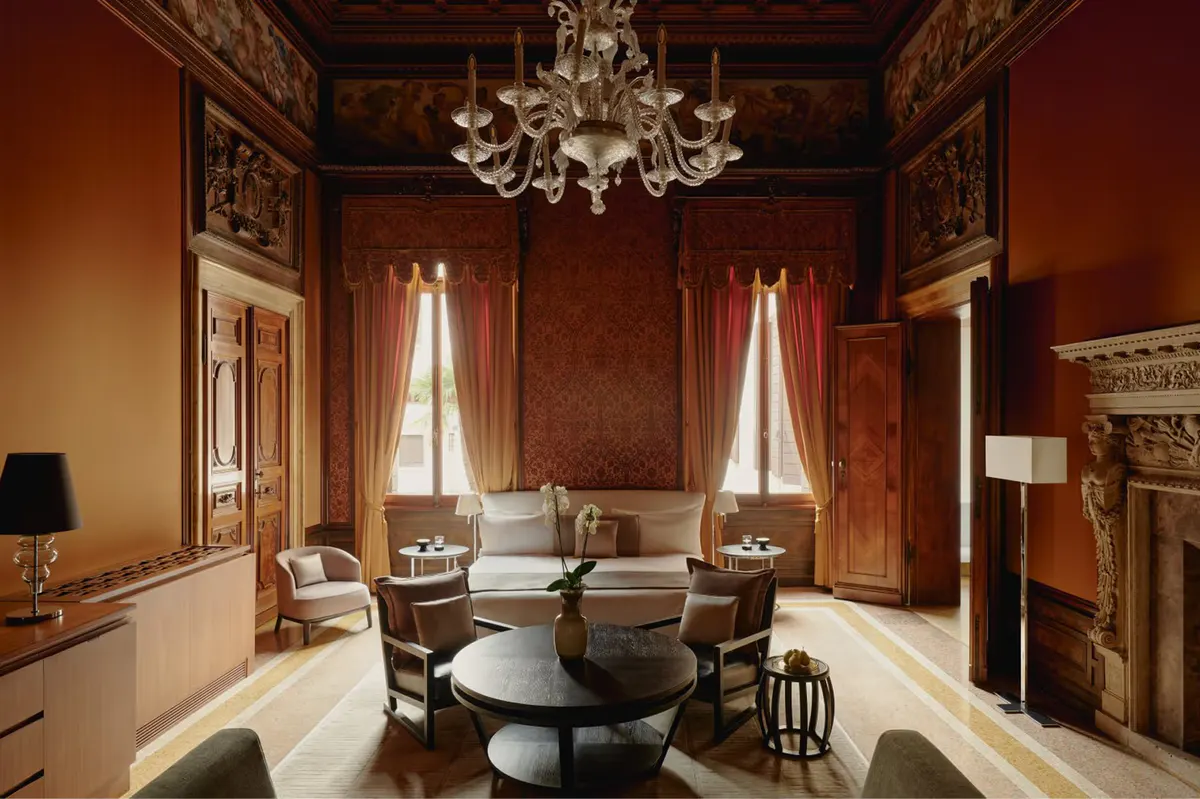 A jewel-toned suite with deep red walls, ornate painted ceiling, white marble fireplace, and cream seating