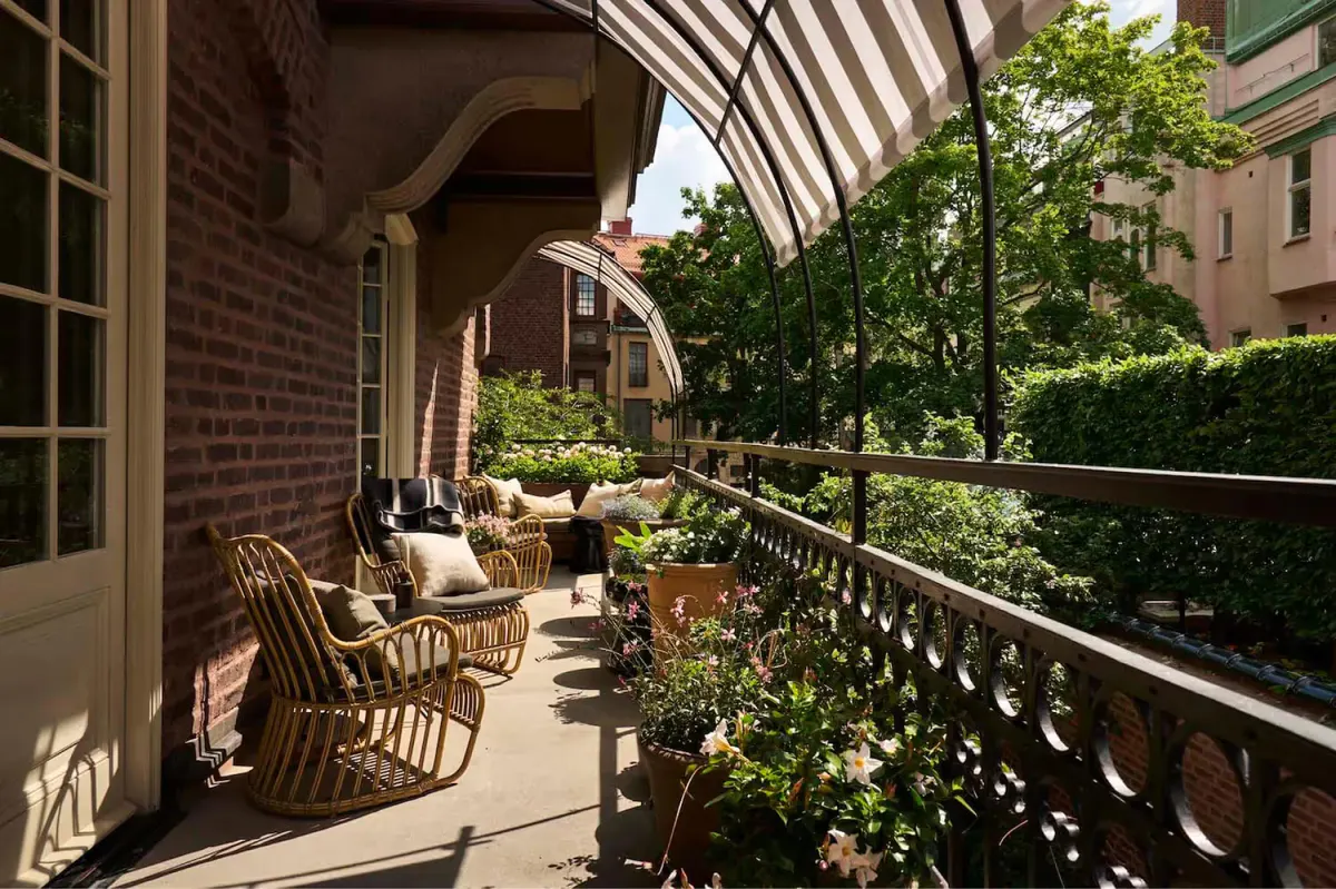 A wooden terrace deck with rattan chairs, iron railings, and mature trees overhead