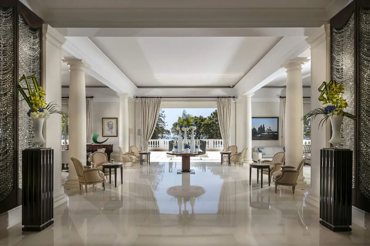 A grand hall with columns, polished floors, and sea views through open doors