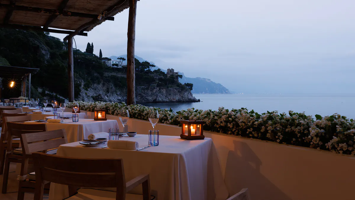 Candlelit dining setup on clifftop terrace at dusk with mountain horizon