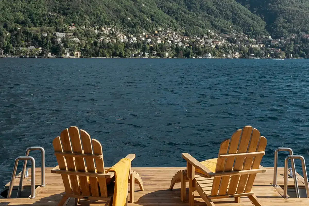 Two wooden Adirondack chairs on a deck facing Lake Como and mountains