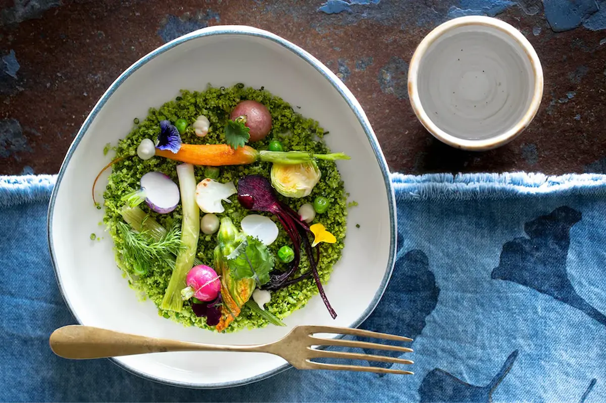 Wellness cuisine plated in white bowl: mixed greens with vegetables and edible flowers on blue tablecloth