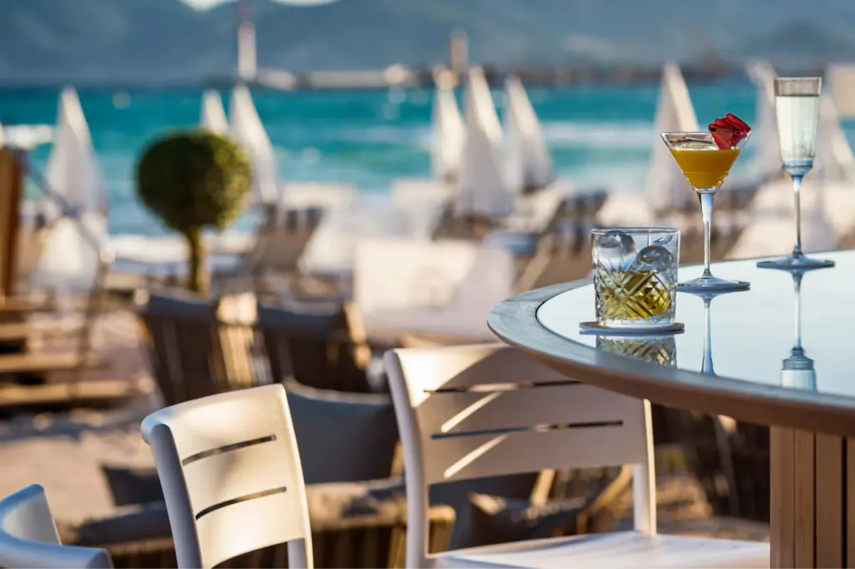 Beachfront dining with a cocktail glass and place setting in foreground overlooking the sand and sea