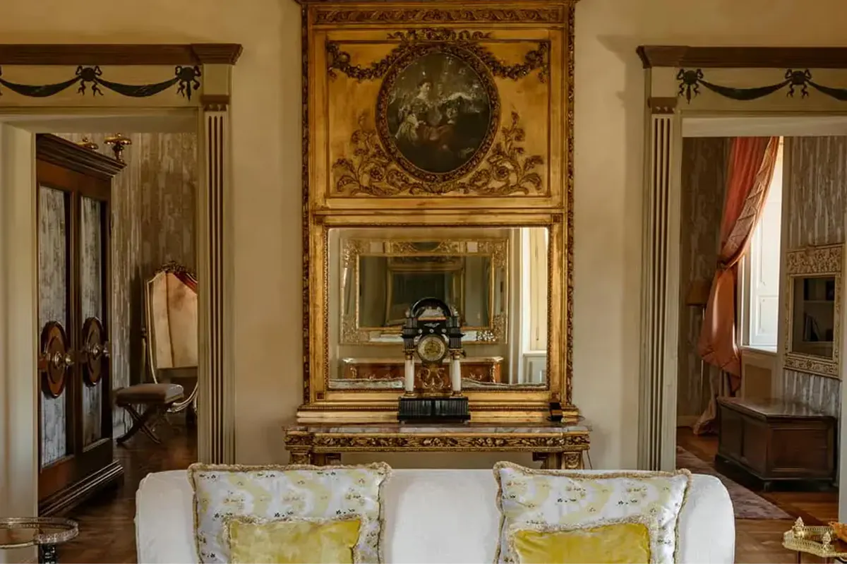 A seating area with ornate gold mirrors, gilded console, and yellow damask cushions