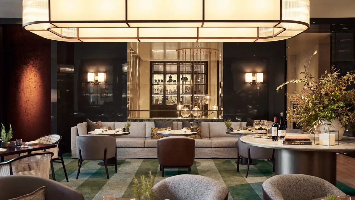 An elegant dining room with gold ceiling detail, dark walls, and formal place settings
