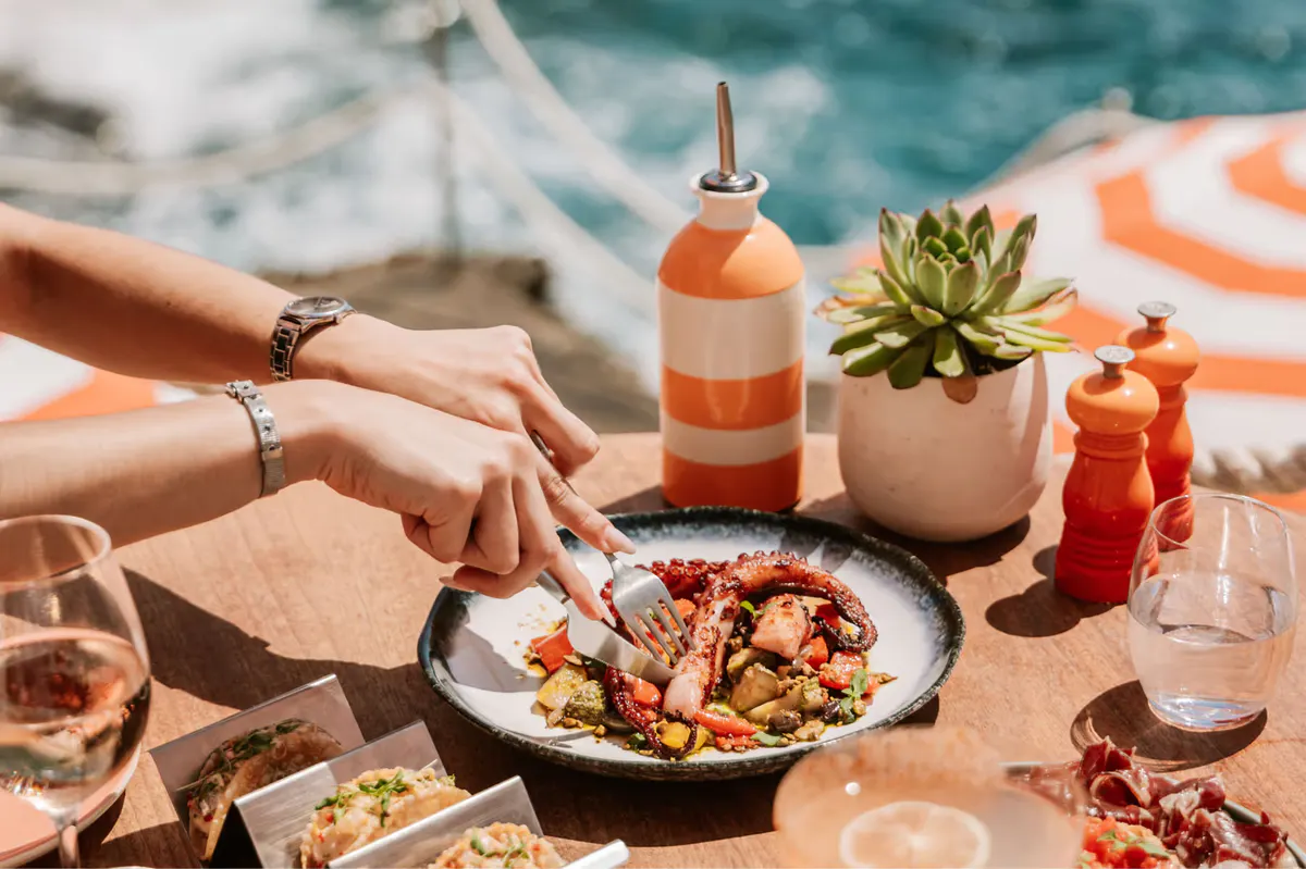 Poolside dining with orange umbrellas and sea backdrop