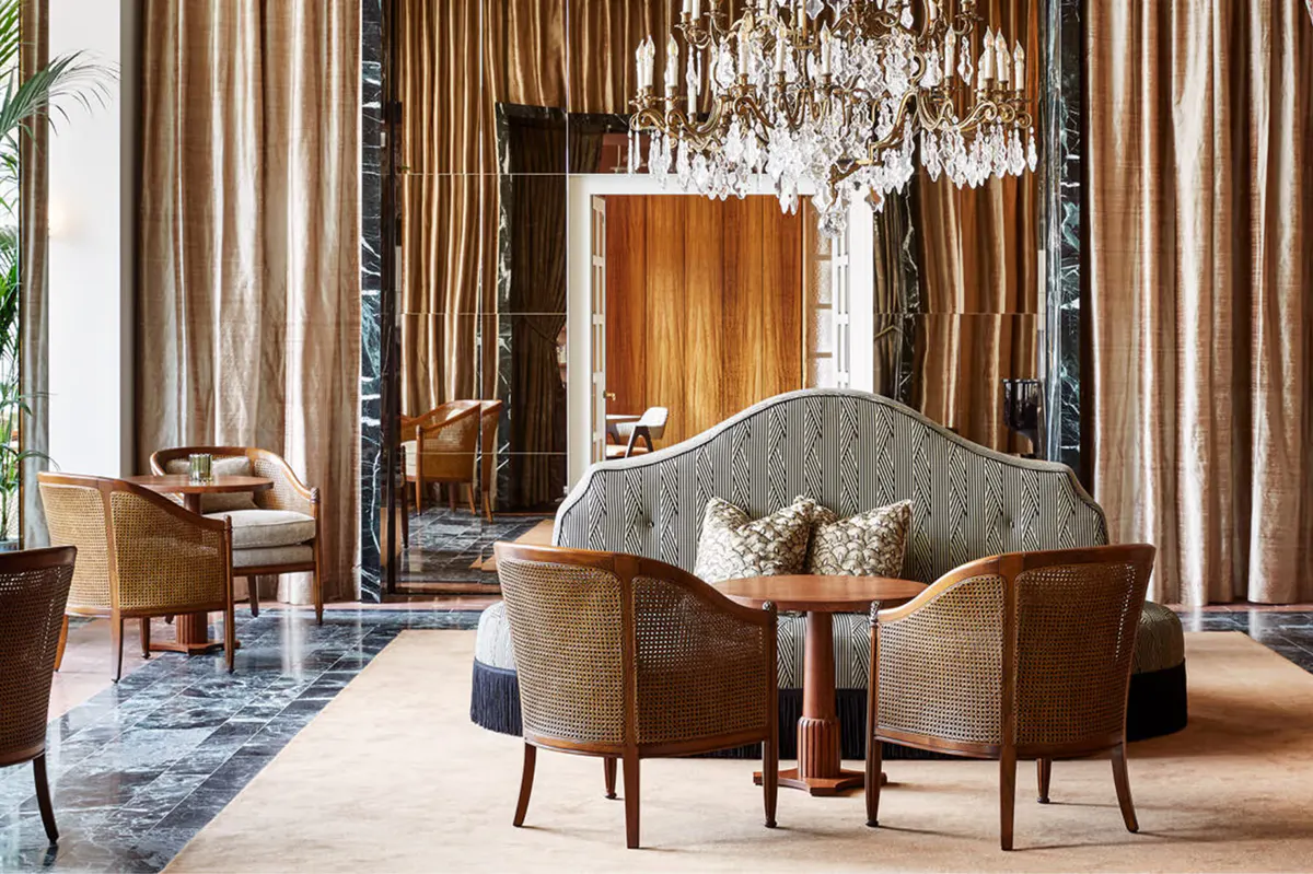 Bedroom with four-poster bed, green velvet upholstered seating, and chandeliers