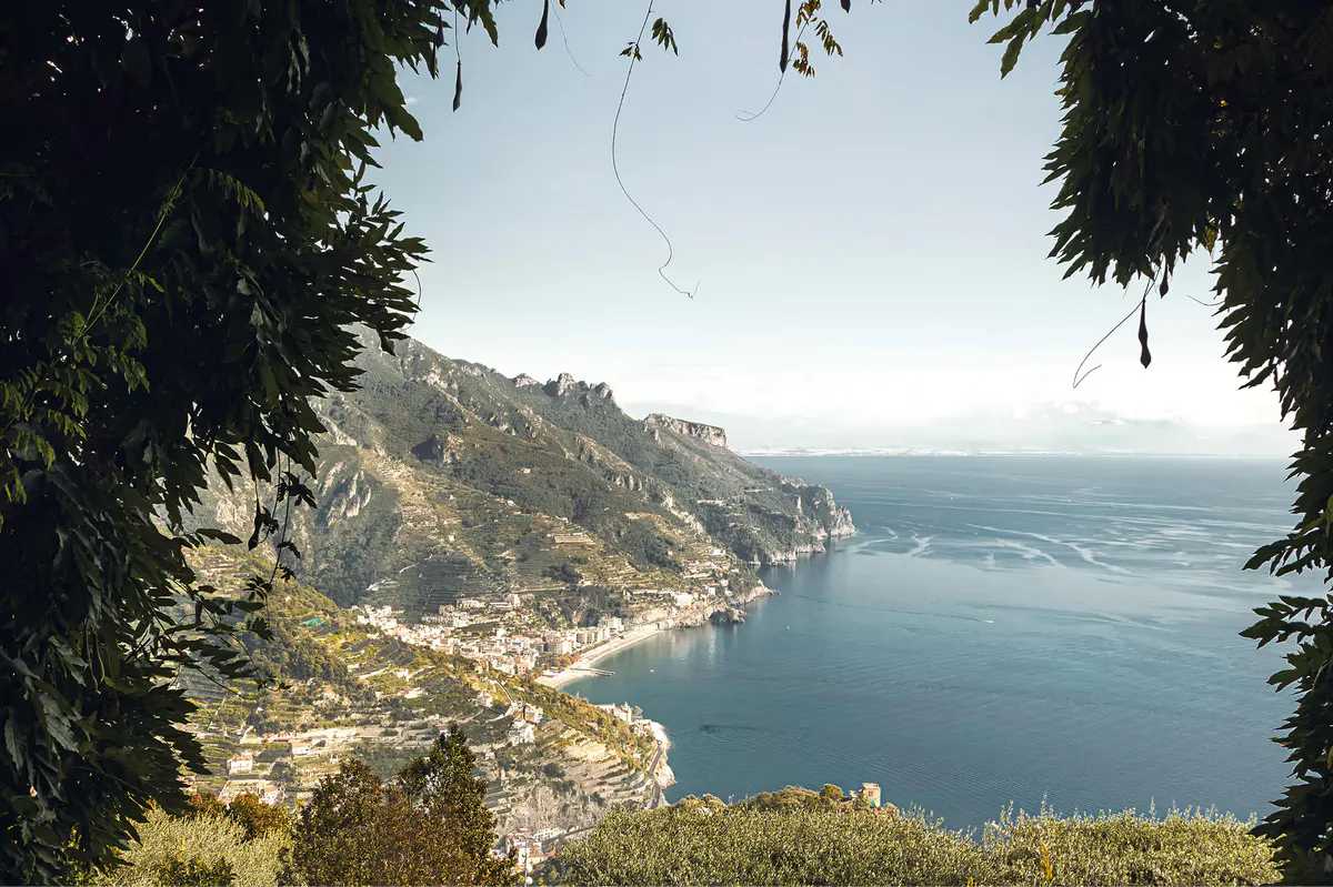 Coastal vista framed by hanging vines, turquoise sea meeting distant rocky hills under bright sky