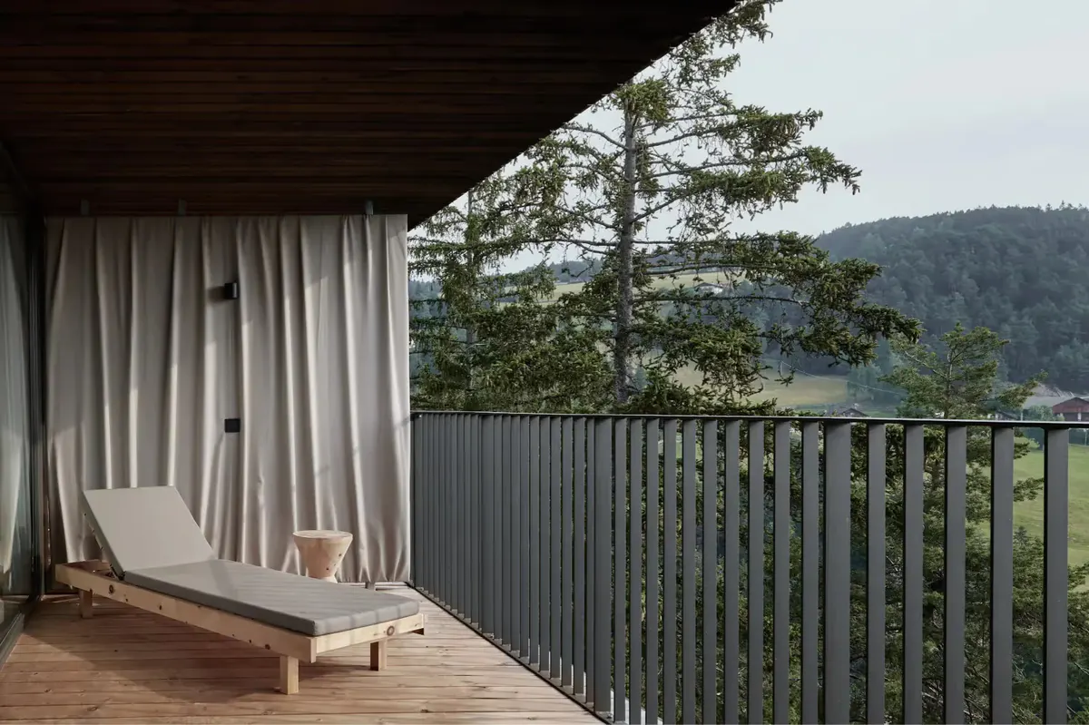 Covered wooden terrace with sheer curtains framing views of pine forest and distant mountains