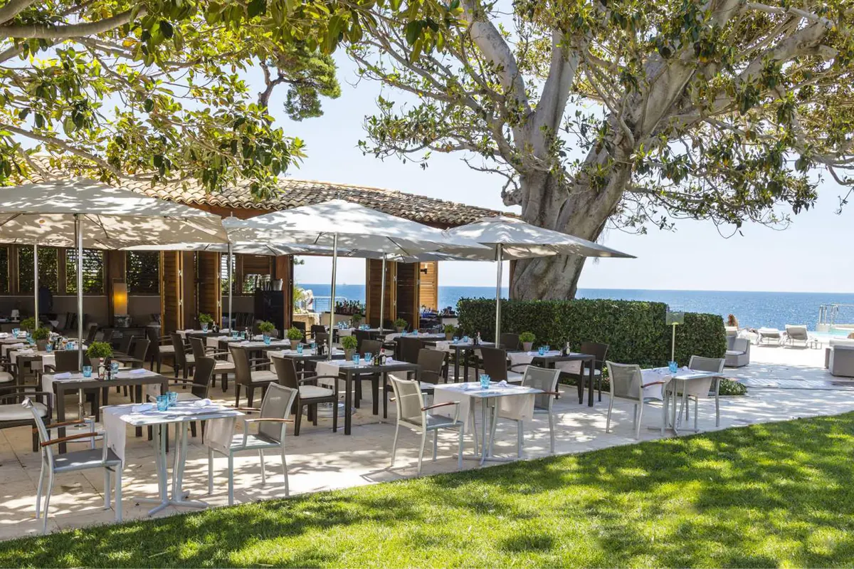 Dining tables arranged under shaded structures with Mediterranean seascape