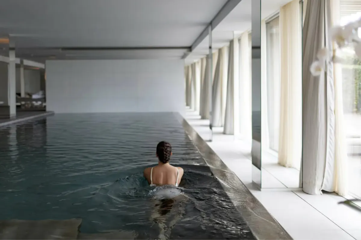 Indoor pool with person swimming in heated water and large windows