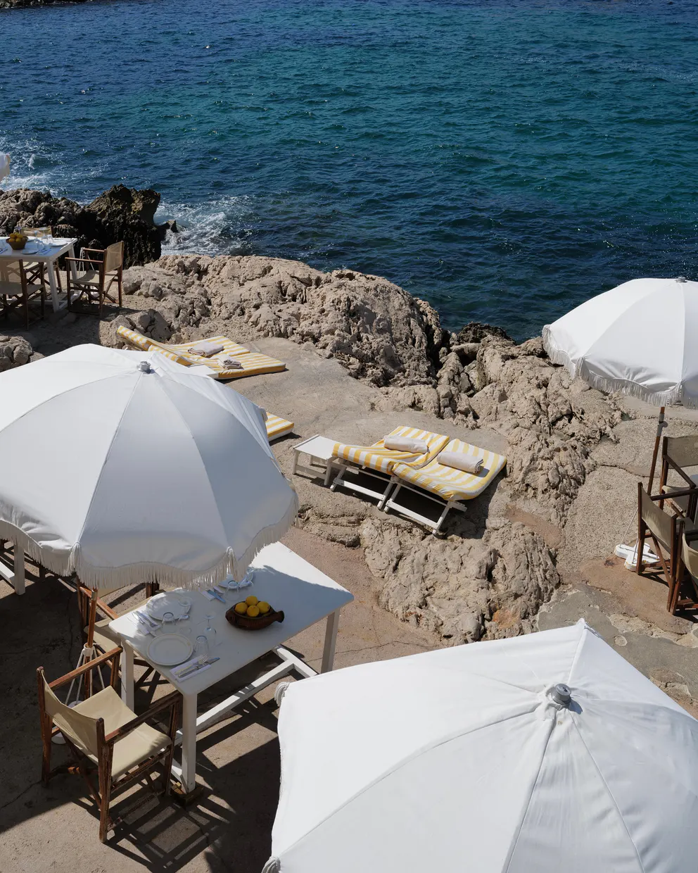 Striped loungers, white parasols and a set table on the rocks at Tuba Club, the sea beyond