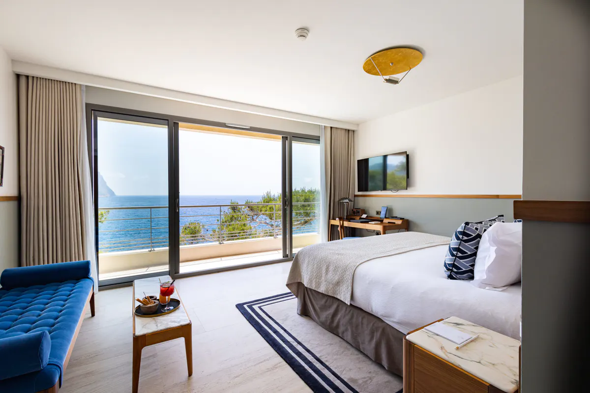 A bedroom with queen bed, floor-to-ceiling windows framing coastal views, and minimal decor