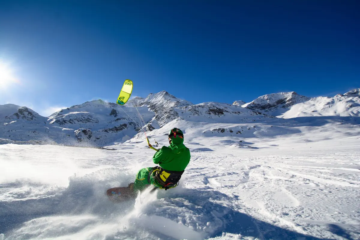 Snowkiter launching off snowy slope with yellow parachute and mountain backdrop