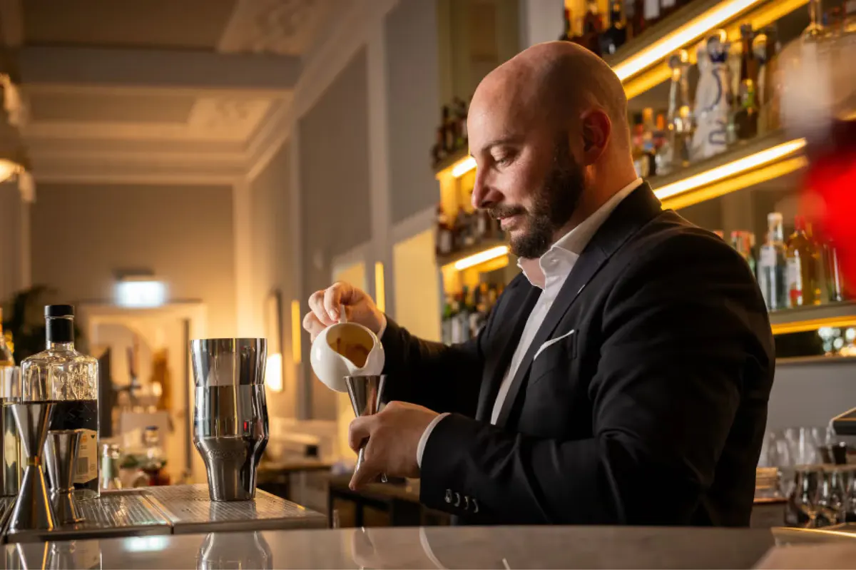 Bartender in suit pouring a drink at an illuminated bar counter