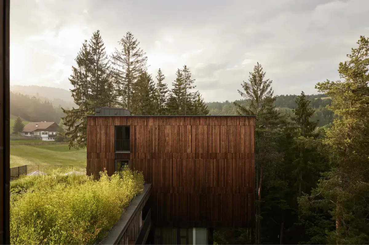 Dark wood building with windows set on hillside overlooking pastoral valley landscape