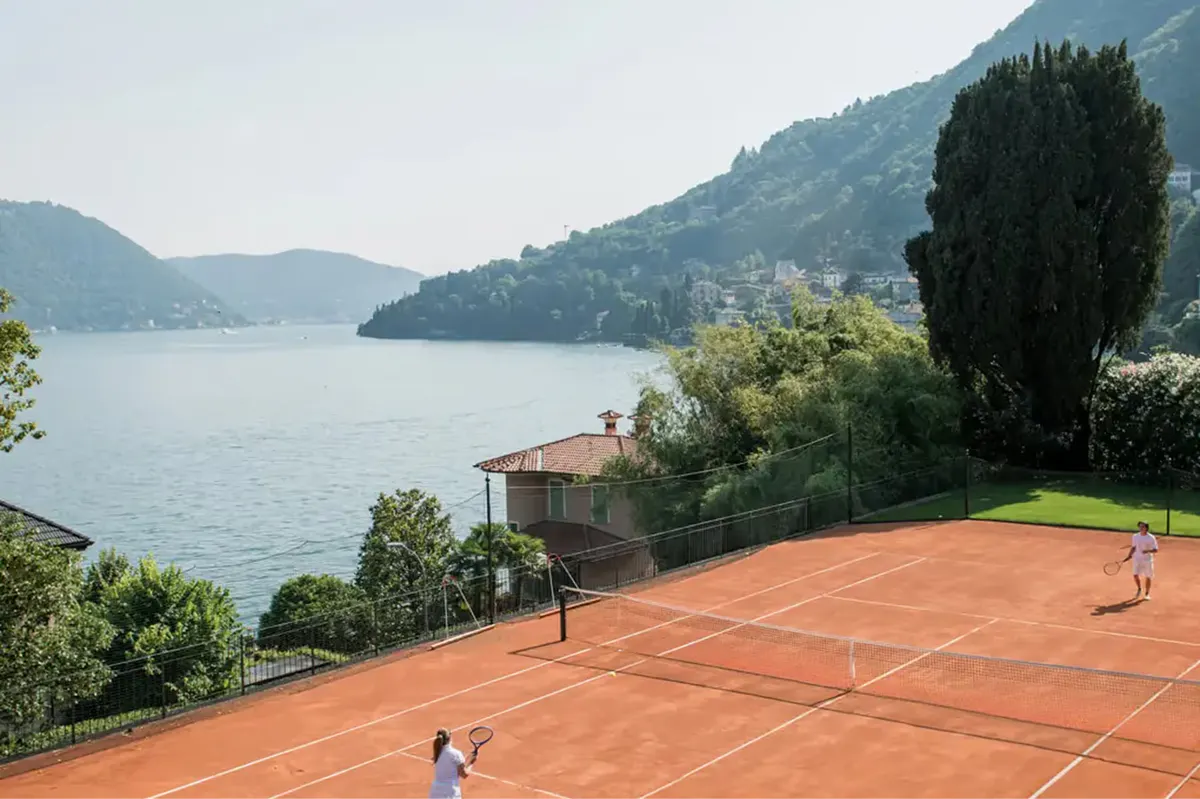 A clay tennis court with lake and mountain scenery on the opposite shore