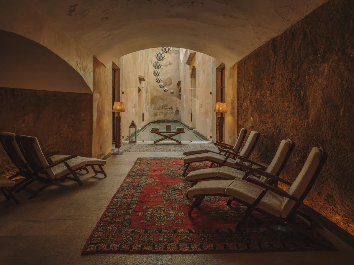 A stone hammam interior with arched ceilings, olive-toned walls, and centered relaxation spaces