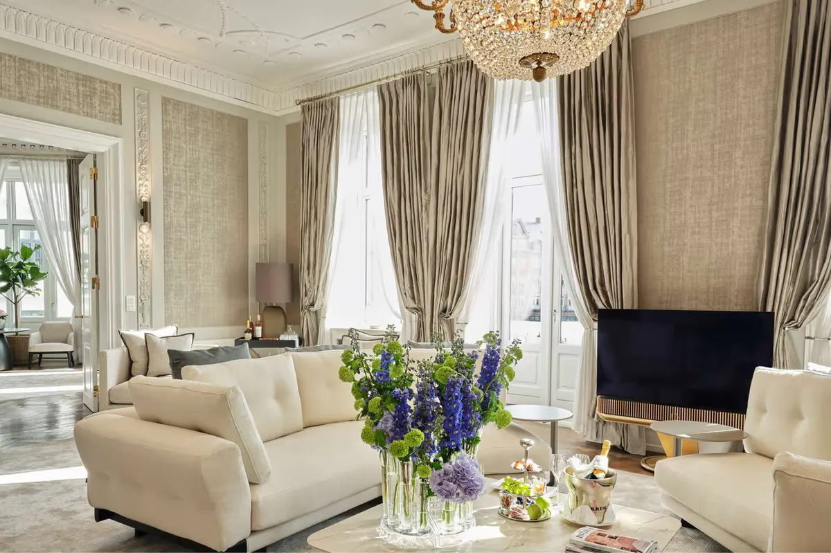 Elegant suite with tall windows, fresh flowers, and cream furnishings