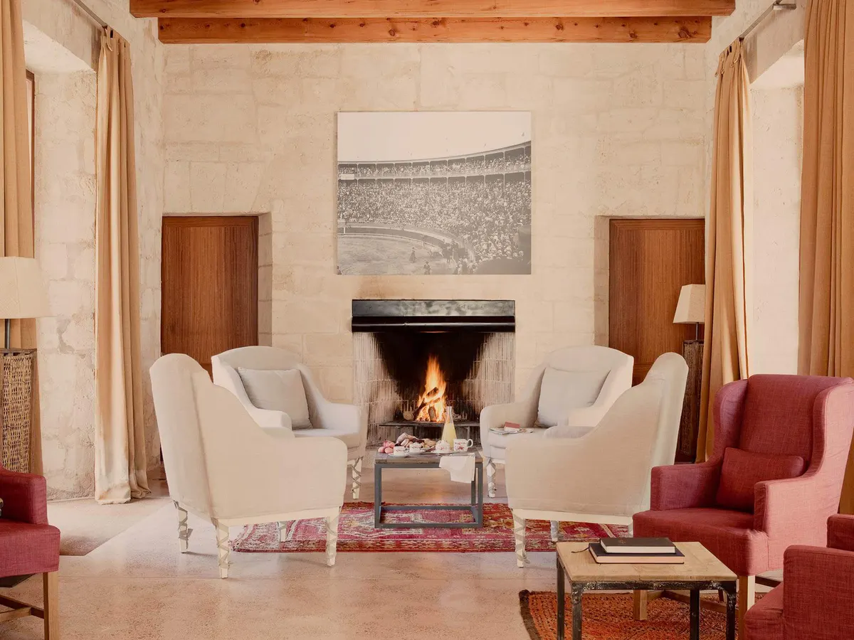 A living room with cream chairs, fireplace, warm wood paneling, and traditional architecture