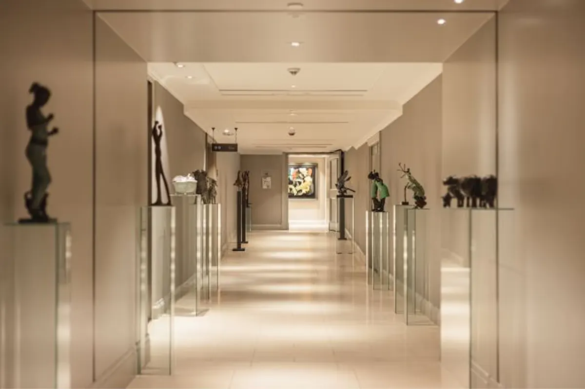 A corridor with glass railings, sculptural pieces displayed on shelves, and soft ambient lighting