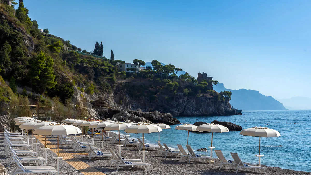 Private beach club with loungers and parasols on pebble shore below cliffs