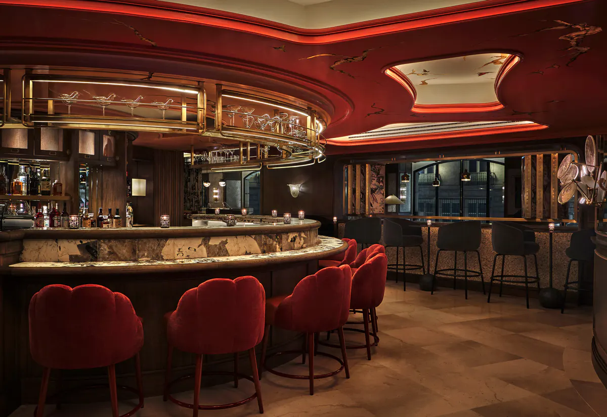 Cocktail bar with deep red upholstered seating, dark wood paneling, brass accents, and amber lighting