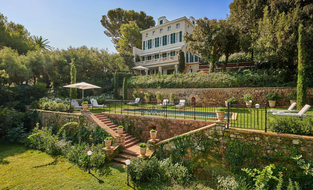 A poolside lounge area with cushioned seating, white umbrellas, and views of the sea and pine trees